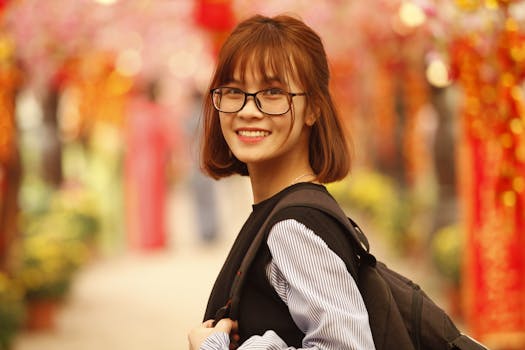 Young woman with glasses and backpack smiling outdoors on a vibrant, festive street.