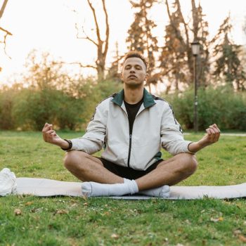 Man meditating outdoors in a tranquil park setting at sunset, promoting relaxation and mindfulness.